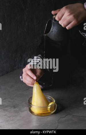 Les mains de l'enfant tenir verseuse et verser le sirop par dessert traditionnel confit de poires au vin blanc dans des bols en verre avec les zestes de citron sur la texture gris table. Banque D'Images