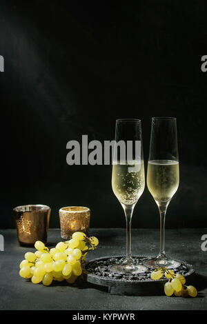Deux verres de champagne servi blanc sur noir décoratif en bois avec des bougies et du raisin vert foncé sur fond de texture. Copy space Banque D'Images