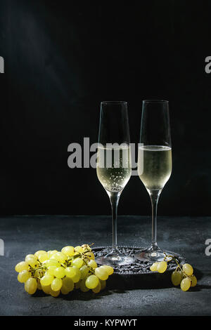 Deux verres de champagne servi blanc sur noir décoratif en bois avec du raisin vert foncé sur fond de texture. Copy space Banque D'Images
