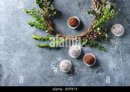 Variété de truffes au chocolat noir faites maison avec de la poudre de cacao, noix de coco, comme cadeau de Noël Décoration avec couronne de Noël sur la texture bleu b Banque D'Images