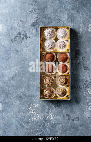 Variété de truffes au chocolat noir faites maison avec de la poudre de cacao, noix de coco, noix dans boîte cadeau doré bleu sur fond de texture. Vue de dessus, copiez l'espace. Banque D'Images