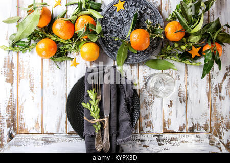 Décorations de table de Noël avec des clémentines ou mandarines avec feuilles et branches vertes sur fond noir fleuri conseil. La plaque vide avec de la vaisselle et du textile Banque D'Images