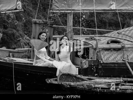 Les jeunes femmes vietnamiennes s'amusant sur une jonque traditionnelle. La baie d'Halong, Vietnam. Ils portent la robe traditionnelle Ao Dai. Banque D'Images