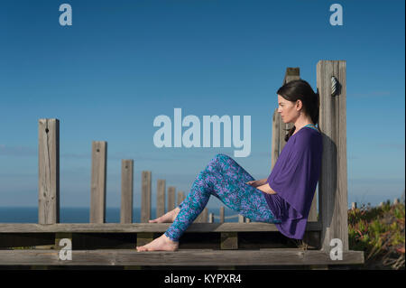 Femme assise sur les marches de bois par la mer, la réflexion et la détente au soleil avoir quelques moi le temps. Banque D'Images