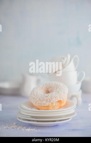 Beignet blanc avec garniture de noix de coco sur un fond clair avec des tasses et soucoupes en porcelaine. High key la photographie culinaire. Pile de vaisselle. Banque D'Images