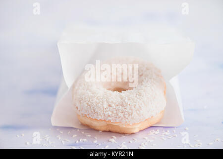 Close-up of a white donut avec coconut topping sur un fond clair à l'intérieur de l'emballage de livraison de papier. High key la photographie culinaire. Banque D'Images