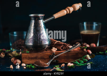 Infuser le café dans cezve. Fond sombre avec des haricots, de la cannelle, noix, feuilles, et broyeur de café. Photo de boissons chaudes. Banque D'Images