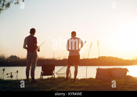 Jeune homme pêche sur le lac au coucher du soleil bénéficiant d'hobby Banque D'Images