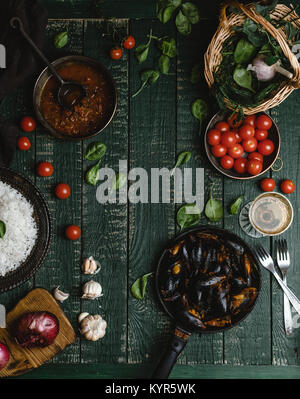 Vue de dessus de moules cuites avec des coquillages servis dans la poêle avec les tomates, les herbes et le vin sur la table rustique Banque D'Images