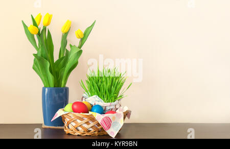 Un panier en osier avec les oeufs de Pâques colorés, tulipes jaunes dans un vase, décoration de Pâques sur fond clair. Espace libre pour votre texte. Banque D'Images