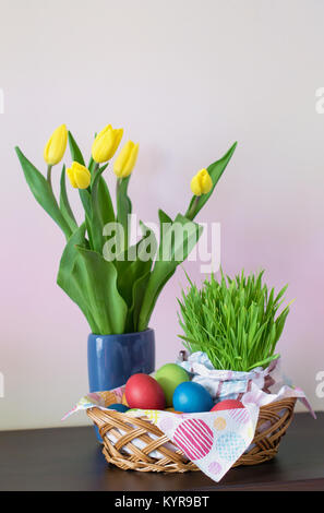 Un panier en osier avec les oeufs de Pâques colorés, tulipes jaunes dans un vase, décoration de Pâques sur fond clair. Espace libre pour votre texte. Banque D'Images