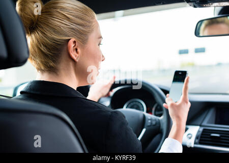 Femme textos sur son téléphone pendant la conduite en voiture Banque D'Images