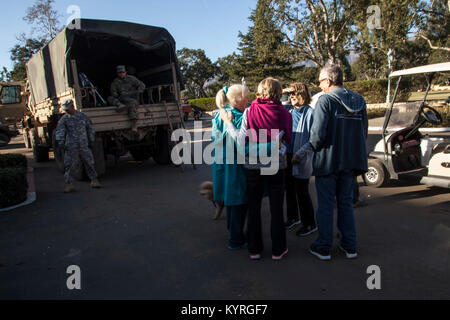 Un groupe de personnes hug en tant que soldats de la Garde nationale de Californie Composite 1114th Transportation Company arrivent à bois Birnam Golf Club à Montecito, en Californie, pour aider les résidents à évacuer un lieu de dépôt centralisé, 11 janvier 2018. Dans les rues de la ville de boue profonde a laissé des quartiers -- y compris le golf club -- coupées des services critiques et les résidents qui l'abri en place pendant une tempête au début de la semaine sont avoir à quitter leurs foyers. Cal légère moyenne garde les véhicules tactiques (LMTVs) sont des véhicules de l'eau avec la possibilité de descendre les routes impraticables pour Banque D'Images