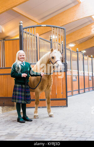 Poney Welsh Mountain, Section A. Girl conduisant un hongre palomino dans une étable lane. Allemagne Banque D'Images