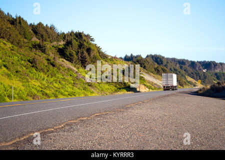 Semi classique avec un camion remorque van sec les feuilles dans la distance au-delà de la ligne d'horizon sur une route isolée avec de l'herbe verte le long de l'océan Pacifique Banque D'Images