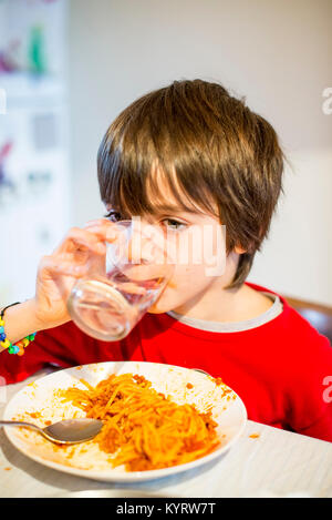 Boire de l'eau et de l'enfant mange du spaghetti à la maison Banque D'Images