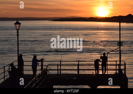 Pêche Les pêcheurs de Victoria Pier, Vieux Portsmouth, Royaume-Uni, silhouetté contre le soleil sur l'île de Wight et de Gosport. Banque D'Images