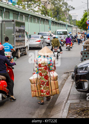 Vie vietnamienne: Femme dans chapeau conique transportant de grands colis sur son dos sur une route animée, vue typique de rue à Saigon (Ho Chi Minh Ville) sud Vietnam Banque D'Images