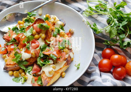 La patate douce cuite méditerranéenne Recette pour Veganuary en utilisant les patates douces, les tomates, les pois chiches, l'hoummos et les herbes. Banque D'Images