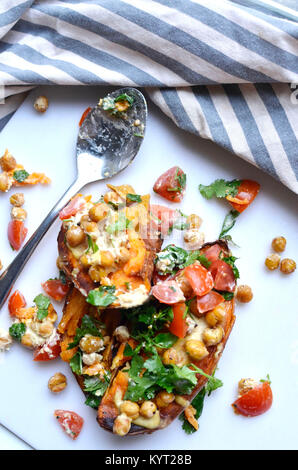 La patate douce cuite méditerranéenne Recette pour Veganuary en utilisant les patates douces, les tomates, les pois chiches, l'hoummos et les herbes. Banque D'Images