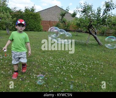 Jeune garçon chasing bubbles in garden Banque D'Images