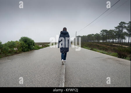 Femme marchant le long d'une route déserte dans la brume et le brouillard Banque D'Images