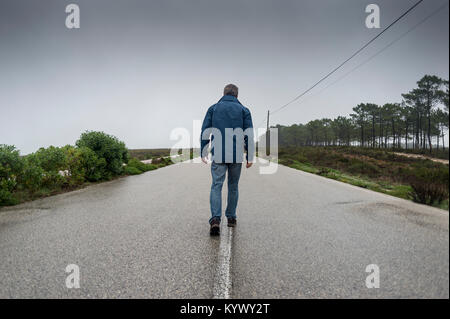 Homme marchant le long d'une route déserte dans la brume et le brouillard Banque D'Images