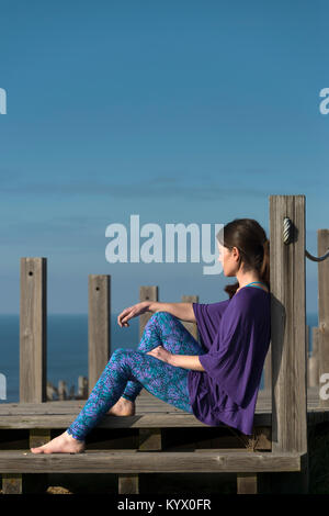 Femme assise sur les marches de bois par la mer, la réflexion et la détente au soleil. Banque D'Images