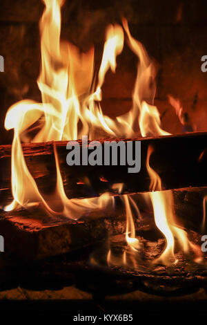 Plusieurs journaux noir, brûlant leurs flammes rouges et d'or à la hausse dans une cheminée sur une froide nuit d'hiver. Close-up vertical coloré mage. Banque D'Images