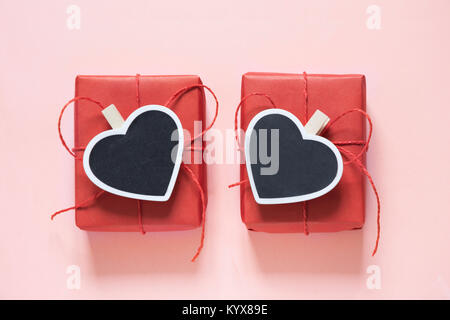 Valentine day composition : deux boîtes cadeau rouge avec clothespin comme cœur de l'espace pour le texte sur tableau noir sur fond rose pastel. Vue d'en haut. Banque D'Images