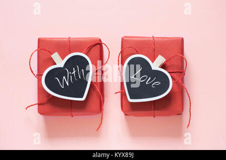 Valentine day composition : deux boîtes cadeau rouge avec clothespin comme coeur avec texte sur tableau noir sur fond rose pastel. Vue d'en haut. Banque D'Images