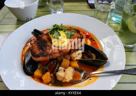 La Bouillabaisse avec du pain grillé servi dans un bol blanc sur une table rustique entouré par des lunettes et un mojito avec un téléphone cellulaire à proximité de pose Banque D'Images