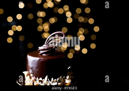 Studio low key horizontal allumé ganache chocolat torte avec bord d'amandes hachées et délicate décoration sculptée sur le dessus. Bokeh lights soft focus. Banque D'Images