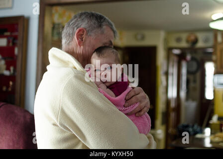 Un grand-père tient sa petite-fille de deux mois dans une couverture rose. Banque D'Images