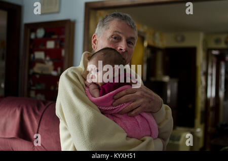 Un grand-père tient sa petite-fille de deux mois dans une couverture rose. Banque D'Images