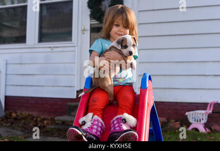 Un bébé fille est titulaire d'un chiot beagle sur une diapositive rouge en été. Banque D'Images