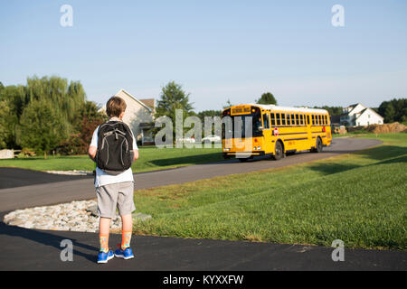 Vue arrière du garçon avec sac à dos en attente pour les autobus scolaires contre ciel clair à lawn Banque D'Images