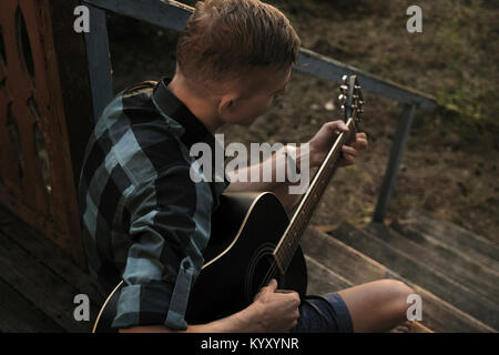 High angle view of man playing guitar while sitting on steps dans porch Banque D'Images