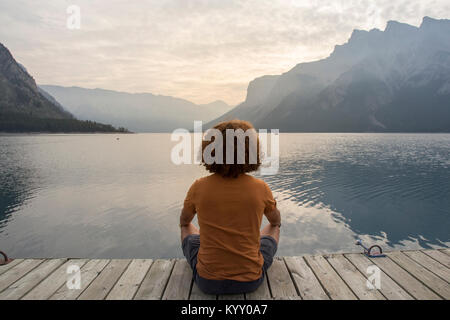 De randonneur while sitting on jetty sur le lac Minnewanka contre montagne Banque D'Images