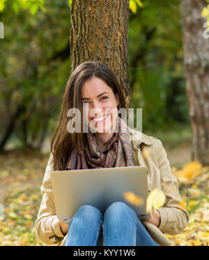 Portrait of smiling woman en position assise par arbre durant l'automne Banque D'Images