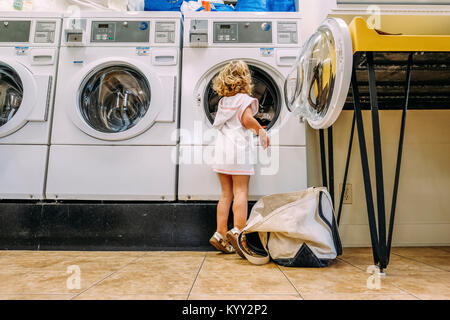 Vue arrière du girl putting vêtements dans le lave-linge à la laverie automatique Banque D'Images