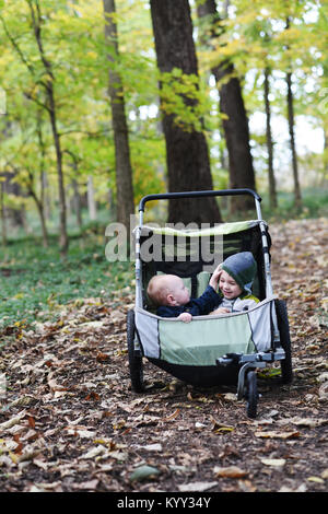 Enfant jouant avec son frère assis en poussette de bébé au parc au cours de l'automne Banque D'Images