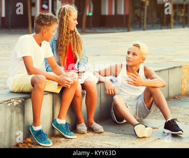 Les enfants adultes heureux de passer du temps ensemble et discuter à l'extérieur à l'aide de téléphones portables Banque D'Images