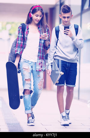 Smiling young friends réalisation skateboards et marche à travers city Banque D'Images