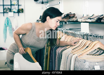 Jeune femme en choisissant Nouveau chemisier à manches longues vêtements en boutique Banque D'Images