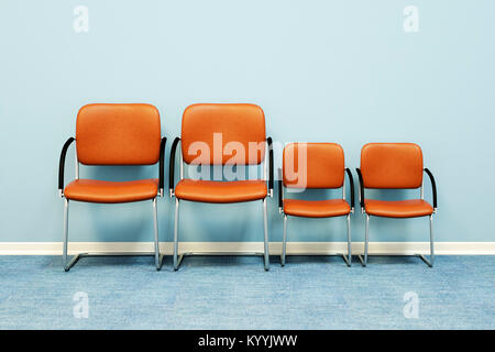 Concept de famille - deux grandes et deux petites chaises dans une rangée contre un mur dans une pièce vide - concept de famille Banque D'Images