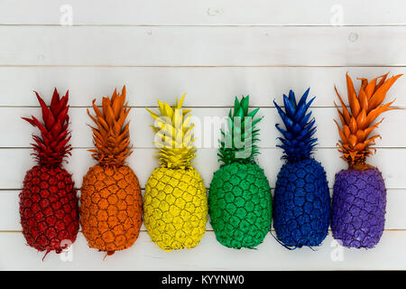 Rangée de vives couleurs arc-en-ciel coloré de l'ananas avec leurs feuilles formant une bordure inférieure sur bois blanc with copy space Banque D'Images