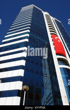 Bâtiment moderne de plusieurs étages de haut avec un grand drapeau turc contre le ciel bleu à Izmir, Turquie. Banque D'Images