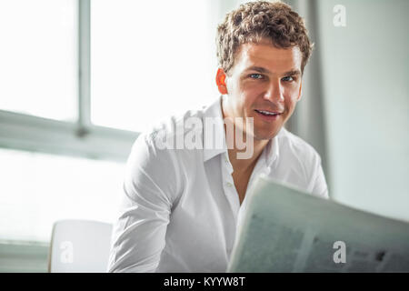 Portrait of handsome young businessman with newspaper in office Banque D'Images