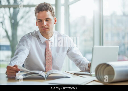 Jeune businessman reading brochure lors de l'utilisation de office Banque D'Images